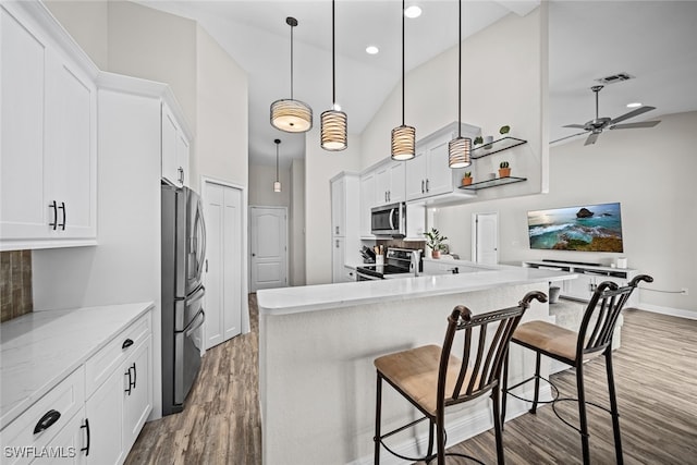 kitchen with dark wood-type flooring, white cabinets, hanging light fixtures, a breakfast bar area, and stainless steel appliances