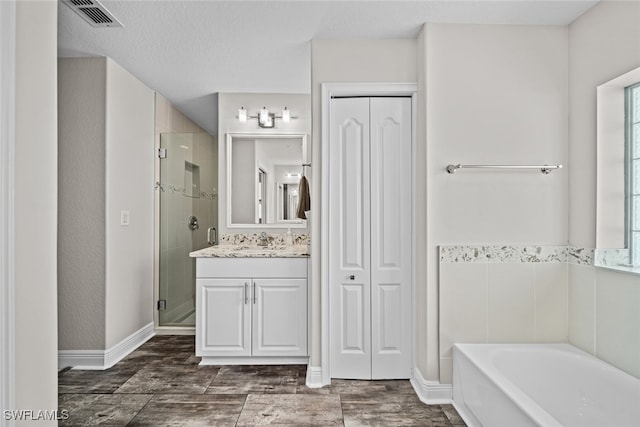 bathroom featuring a textured ceiling, vanity, and shower with separate bathtub