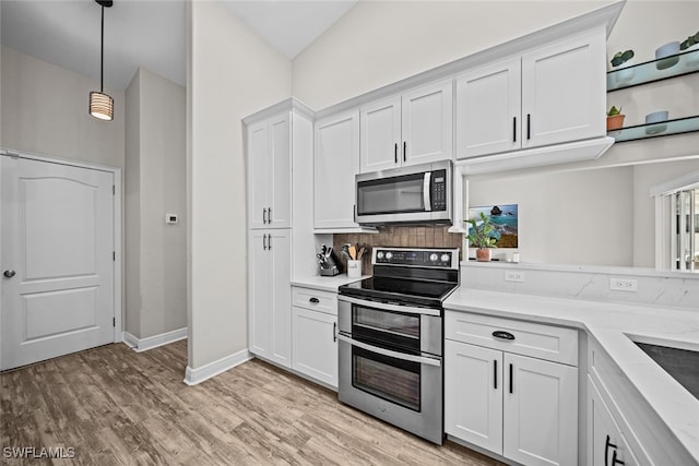 kitchen with stainless steel appliances, vaulted ceiling, pendant lighting, light hardwood / wood-style floors, and white cabinetry