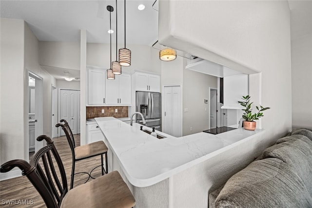 kitchen with high vaulted ceiling, kitchen peninsula, stainless steel fridge, a kitchen bar, and white cabinetry