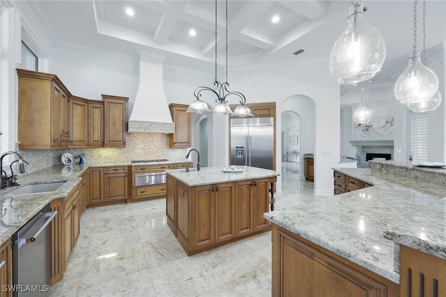 kitchen featuring premium range hood, a center island with sink, appliances with stainless steel finishes, decorative light fixtures, and sink