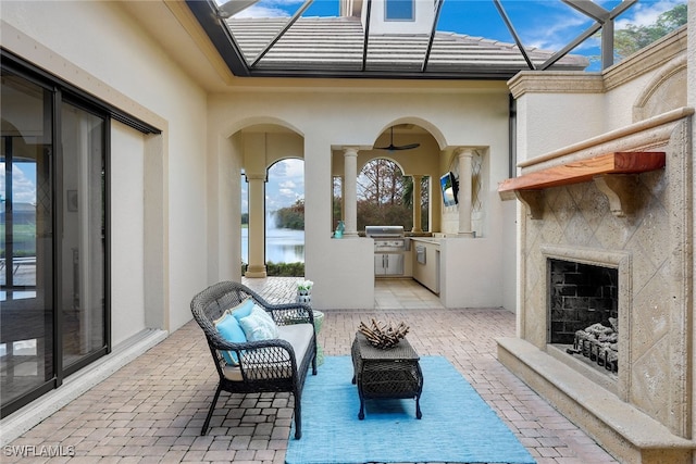 view of patio / terrace with grilling area, an outdoor fireplace, glass enclosure, and exterior kitchen