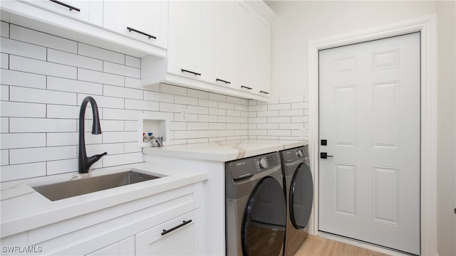 laundry area featuring sink, washer and clothes dryer, light wood-type flooring, and cabinets