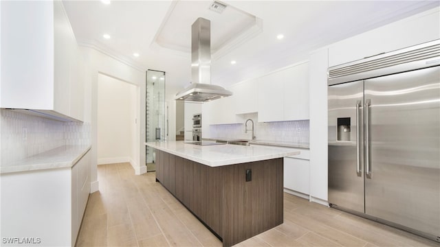 kitchen featuring appliances with stainless steel finishes, white cabinetry, island range hood, light wood-type flooring, and a center island