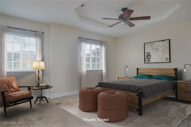 bedroom featuring a raised ceiling, light colored carpet, and ceiling fan