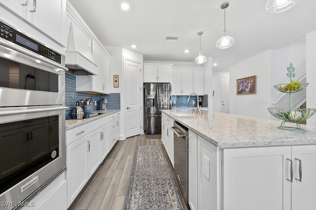 kitchen with sink, light hardwood / wood-style floors, stainless steel appliances, white cabinets, and a kitchen island with sink