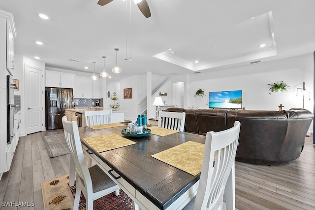 dining room with sink, a tray ceiling, light wood-type flooring, and ceiling fan