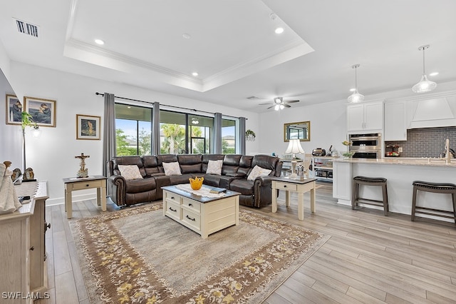 living room with ceiling fan, a raised ceiling, and light wood-type flooring