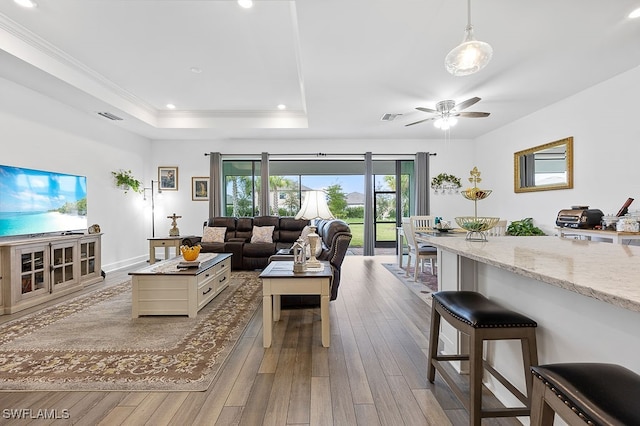 living room featuring light hardwood / wood-style floors, crown molding, a tray ceiling, and ceiling fan