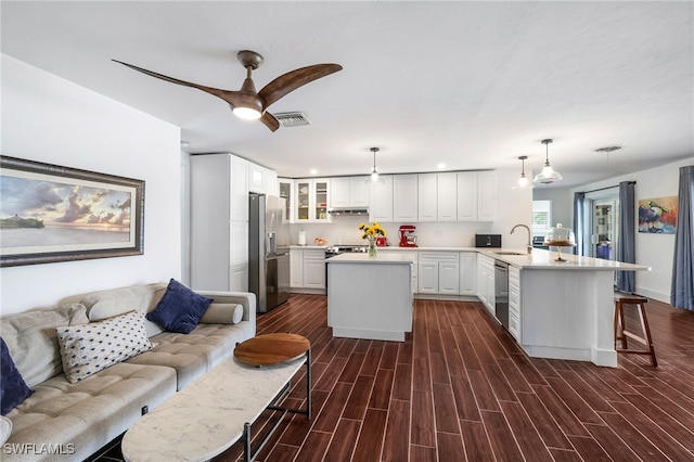 kitchen with an island with sink, white cabinetry, stainless steel appliances, pendant lighting, and dark hardwood / wood-style floors