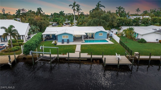 back house at dusk with a patio, a water view, a fenced in pool, and a lawn