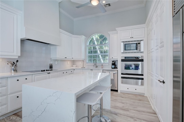 kitchen with backsplash, built in appliances, light stone countertops, a kitchen island, and white cabinetry