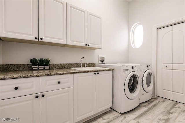 laundry room with cabinets, sink, washing machine and dryer, and light hardwood / wood-style flooring