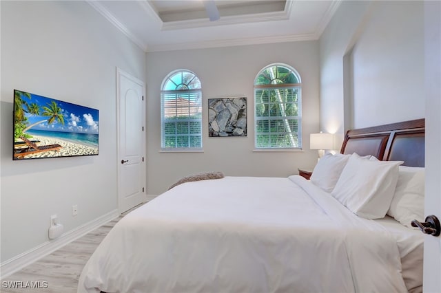 bedroom with light wood-type flooring, crown molding, and a tray ceiling