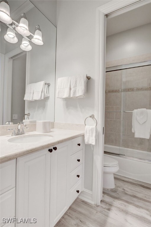 full bathroom with toilet, hardwood / wood-style floors, vanity, and combined bath / shower with glass door