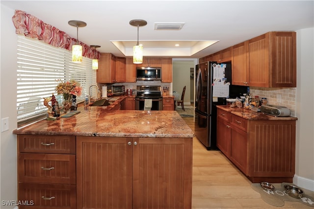 kitchen featuring kitchen peninsula, a raised ceiling, stainless steel appliances, light hardwood / wood-style floors, and decorative light fixtures