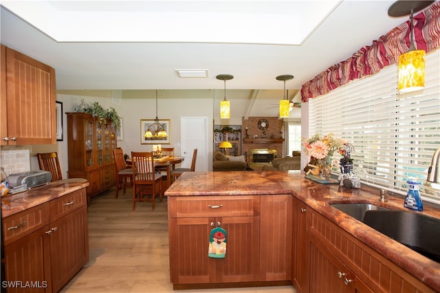 kitchen with light hardwood / wood-style flooring, sink, a brick fireplace, pendant lighting, and tasteful backsplash