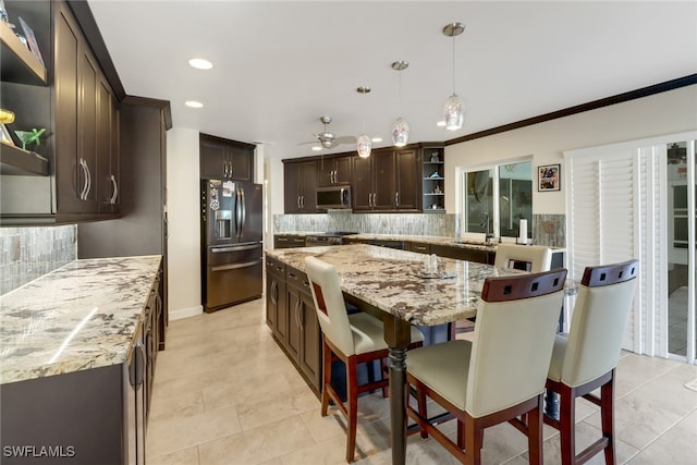 kitchen featuring backsplash, a center island, decorative light fixtures, appliances with stainless steel finishes, and light stone counters