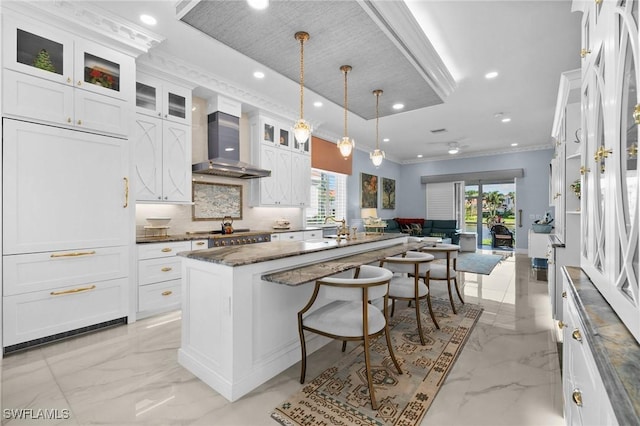 kitchen featuring white cabinetry, wall chimney range hood, pendant lighting, a breakfast bar area, and a kitchen island