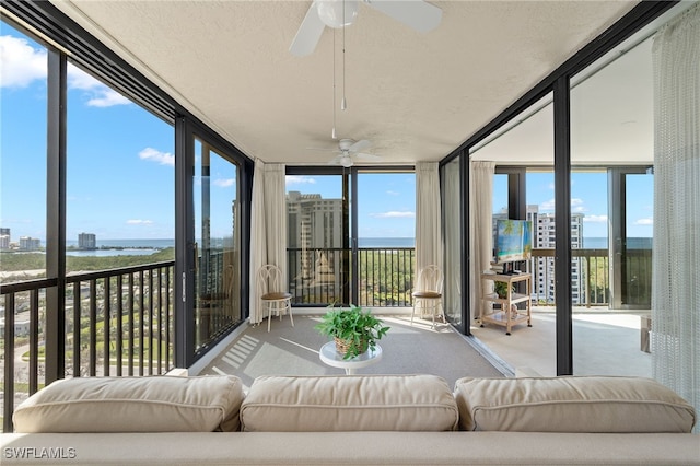sunroom / solarium with a water view, a ceiling fan, plenty of natural light, and carpet flooring