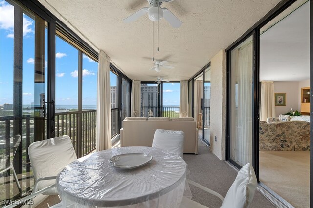 sunroom featuring carpet floors, a textured ceiling, a water view, and a wall of windows