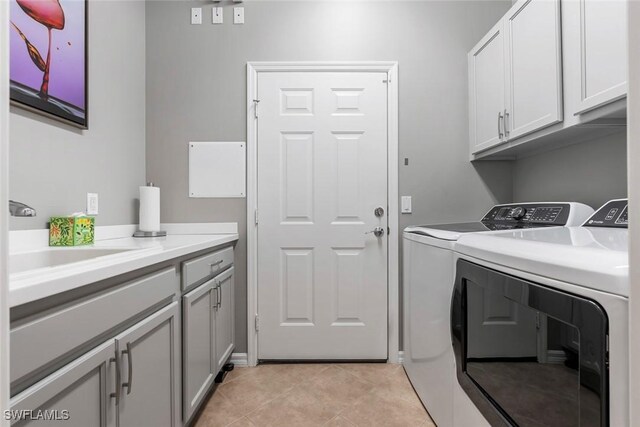 laundry room with sink, washing machine and clothes dryer, light tile patterned floors, and cabinets