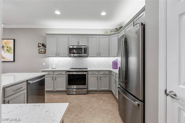 kitchen featuring gray cabinetry, light stone countertops, appliances with stainless steel finishes, backsplash, and crown molding