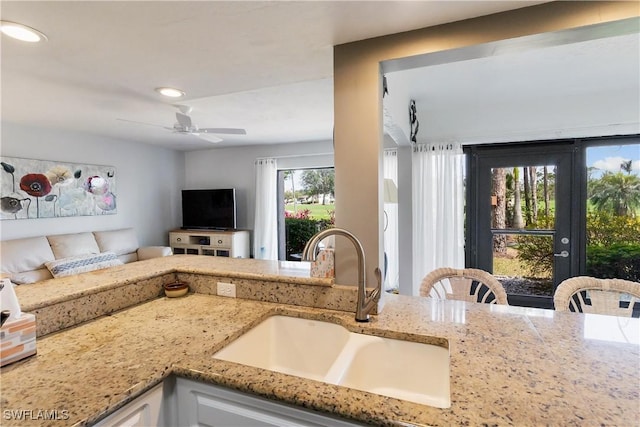 kitchen featuring light stone counters, ceiling fan, and sink