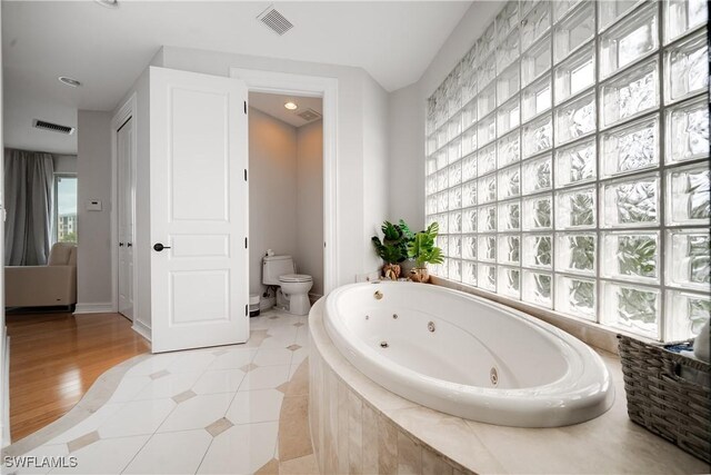 bathroom with hardwood / wood-style floors, a relaxing tiled tub, and toilet