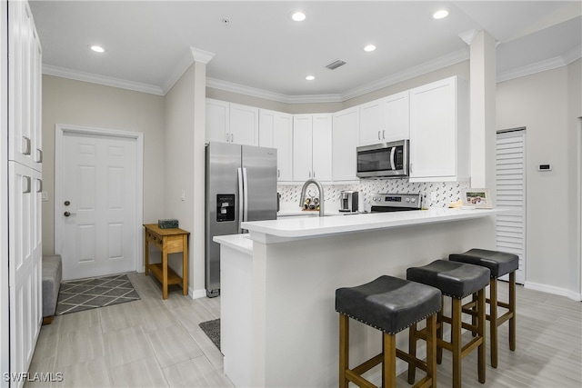 kitchen with white cabinets, appliances with stainless steel finishes, tasteful backsplash, kitchen peninsula, and a breakfast bar area