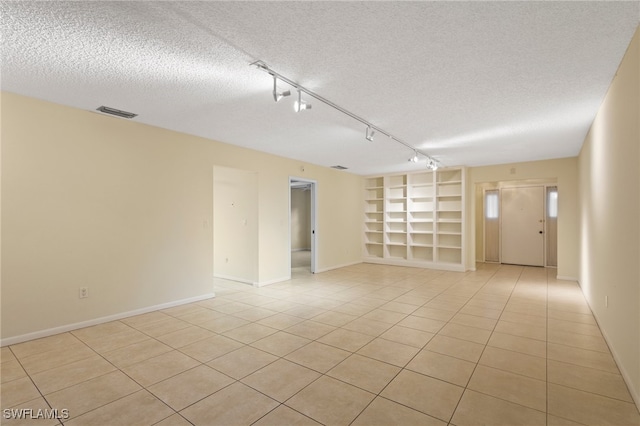 spare room with built in features, rail lighting, a textured ceiling, and light tile patterned flooring