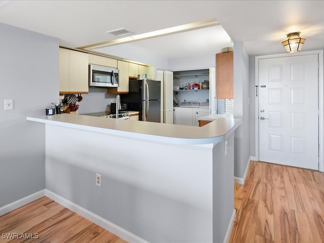 kitchen with stainless steel appliances, washing machine and dryer, light wood-type flooring, and kitchen peninsula