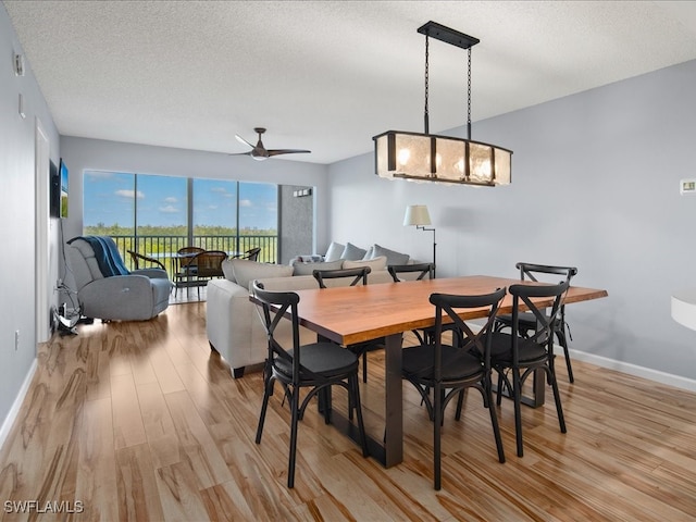 dining room with light wood-type flooring, ceiling fan with notable chandelier, and a textured ceiling