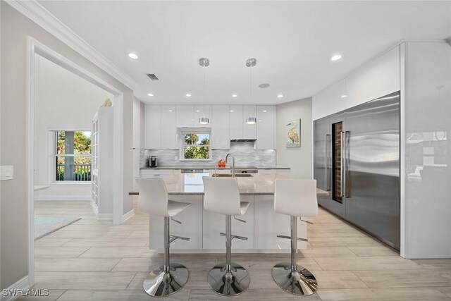 kitchen with pendant lighting, a breakfast bar, stainless steel built in fridge, light stone countertops, and white cabinetry