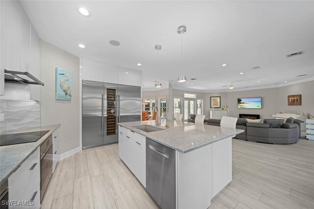 kitchen with white cabinets, stainless steel appliances, a kitchen island with sink, and ceiling fan