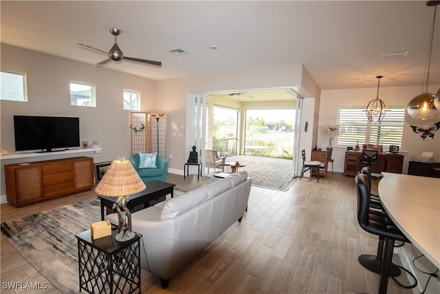 living room featuring ceiling fan with notable chandelier, plenty of natural light, and light wood-type flooring