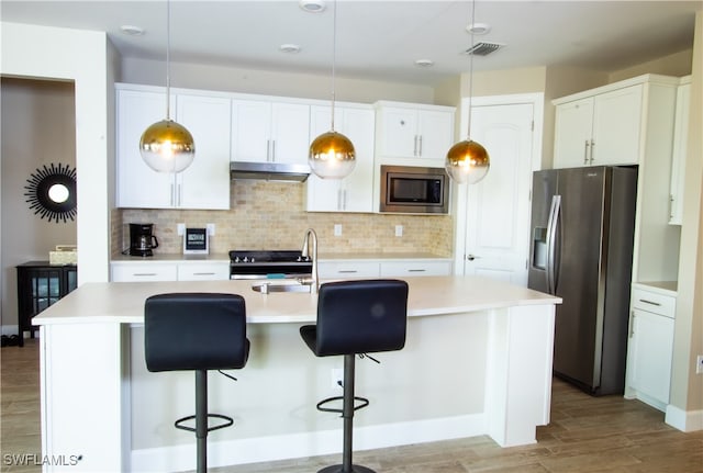 kitchen featuring a kitchen island with sink, stainless steel appliances, decorative light fixtures, light wood-type flooring, and white cabinets