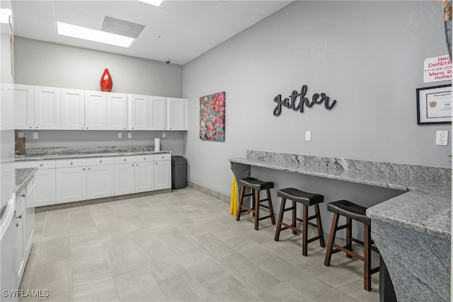 kitchen with a kitchen breakfast bar, white cabinetry, and light stone countertops