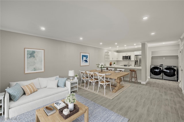 living room with washer and dryer, light hardwood / wood-style flooring, ornamental molding, and sink