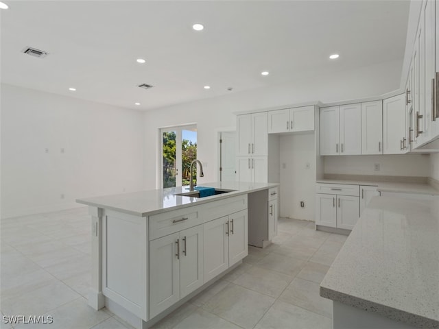 kitchen featuring white cabinetry, sink, light stone counters, and an island with sink