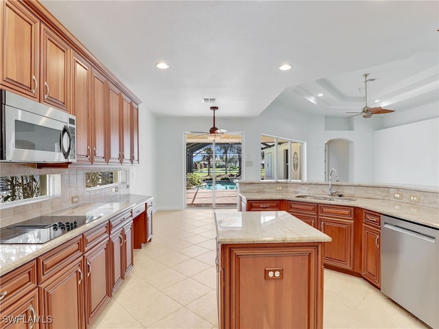 kitchen featuring hanging light fixtures, light stone counters, a kitchen island, appliances with stainless steel finishes, and sink