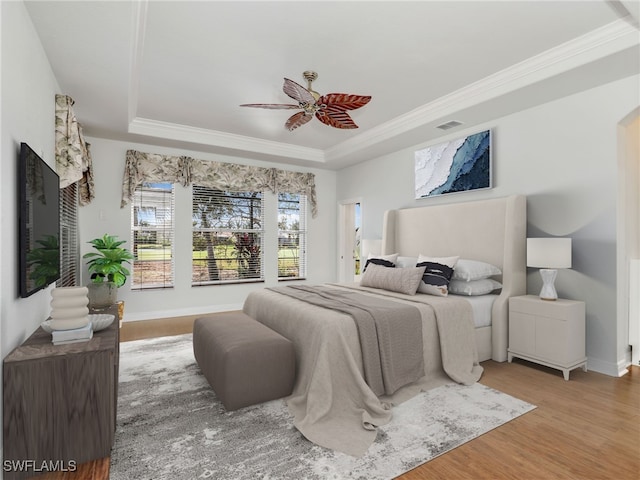 bedroom with ceiling fan, crown molding, wood-type flooring, and a tray ceiling