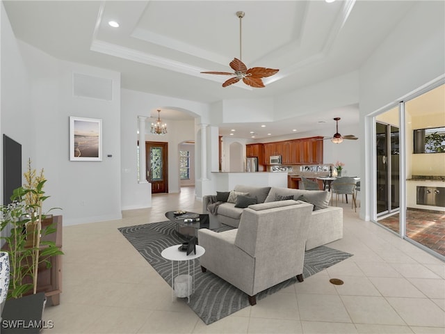 tiled living room with a high ceiling, ceiling fan, decorative columns, and a raised ceiling