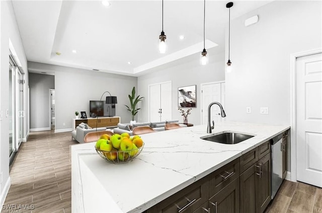 kitchen with hanging light fixtures, sink, light stone counters, and a tray ceiling