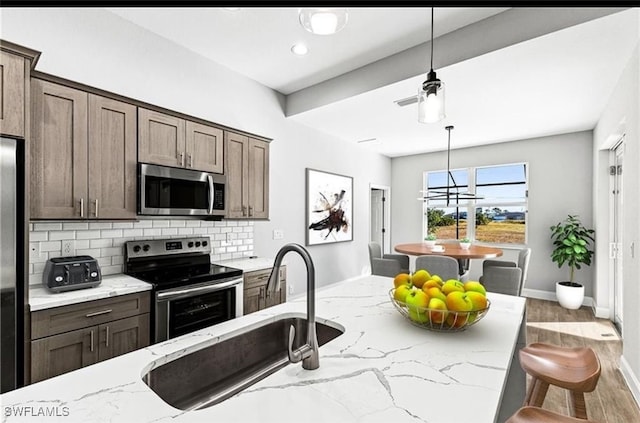 kitchen with tasteful backsplash, light stone counters, stainless steel appliances, sink, and a breakfast bar area