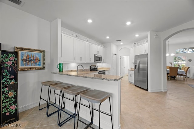 kitchen with kitchen peninsula, light stone countertops, light tile patterned flooring, white cabinetry, and appliances with stainless steel finishes