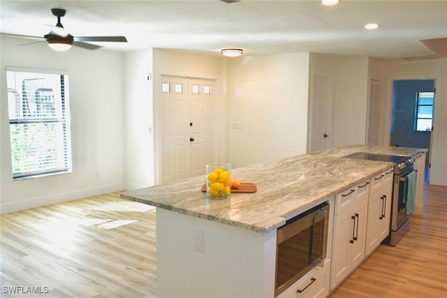 kitchen with light stone countertops, stainless steel appliances, white cabinetry, and light hardwood / wood-style flooring