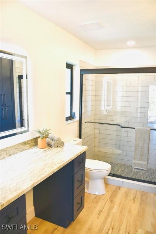 bathroom with hardwood / wood-style floors, vanity, a shower with shower door, and toilet