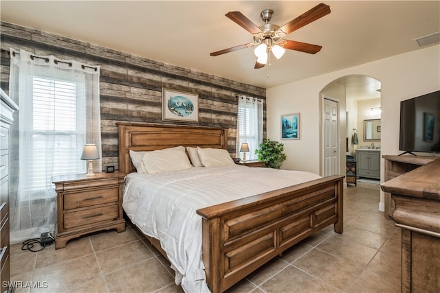 bedroom with wood walls, ensuite bathroom, ceiling fan, light tile patterned flooring, and a closet