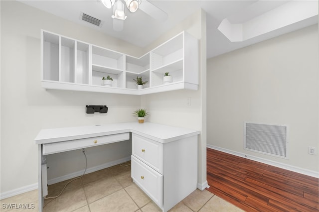 unfurnished office with ceiling fan, built in desk, and light wood-type flooring